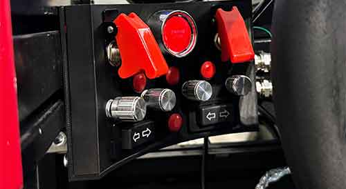 Close-up of a sim racing control panel featuring toggle switches, engine start button and rotary knobs